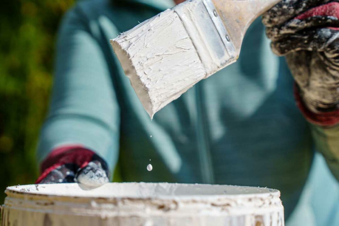 Un pinceau sort d'un pot de peinture blanche.