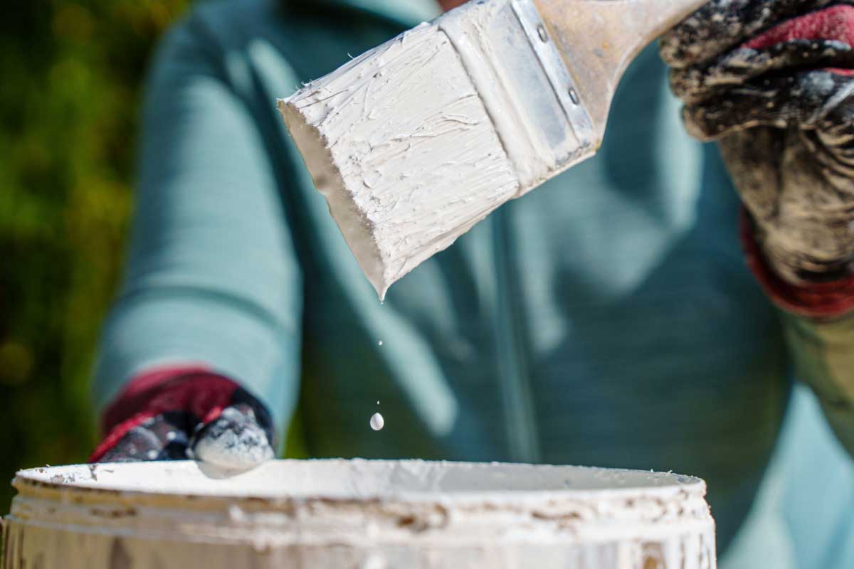 Un pinceau sort d'un pot de peinture blanche.