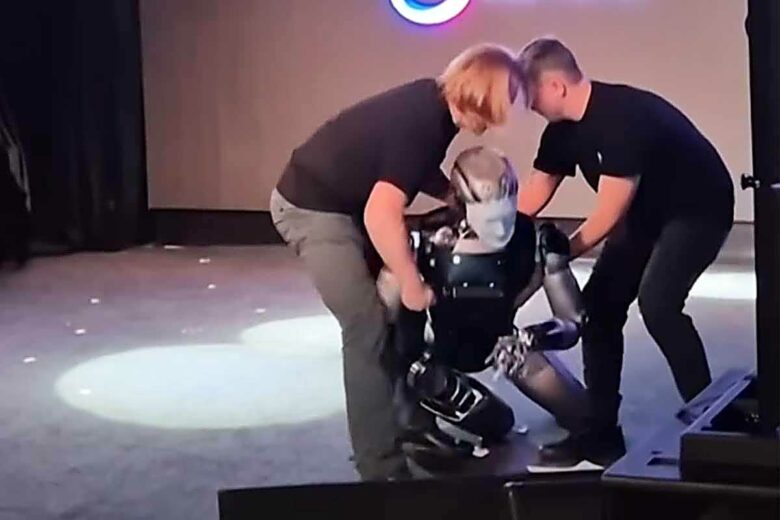 Deux hommes relèvent le robot Aidol.