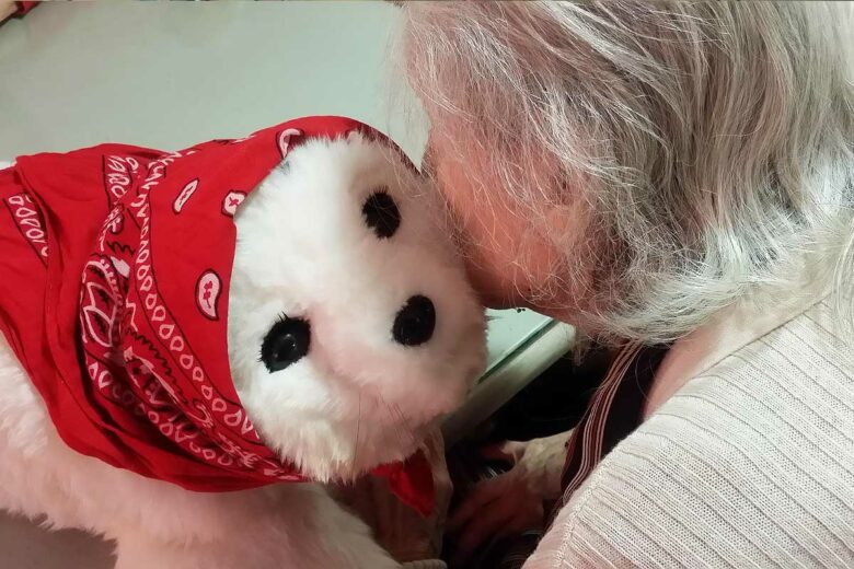 Une personne âgée serre le robot Paro contre sa joue.