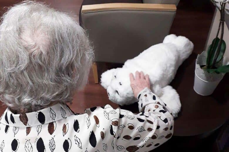 Une personne agée caresse le phoque Paro.