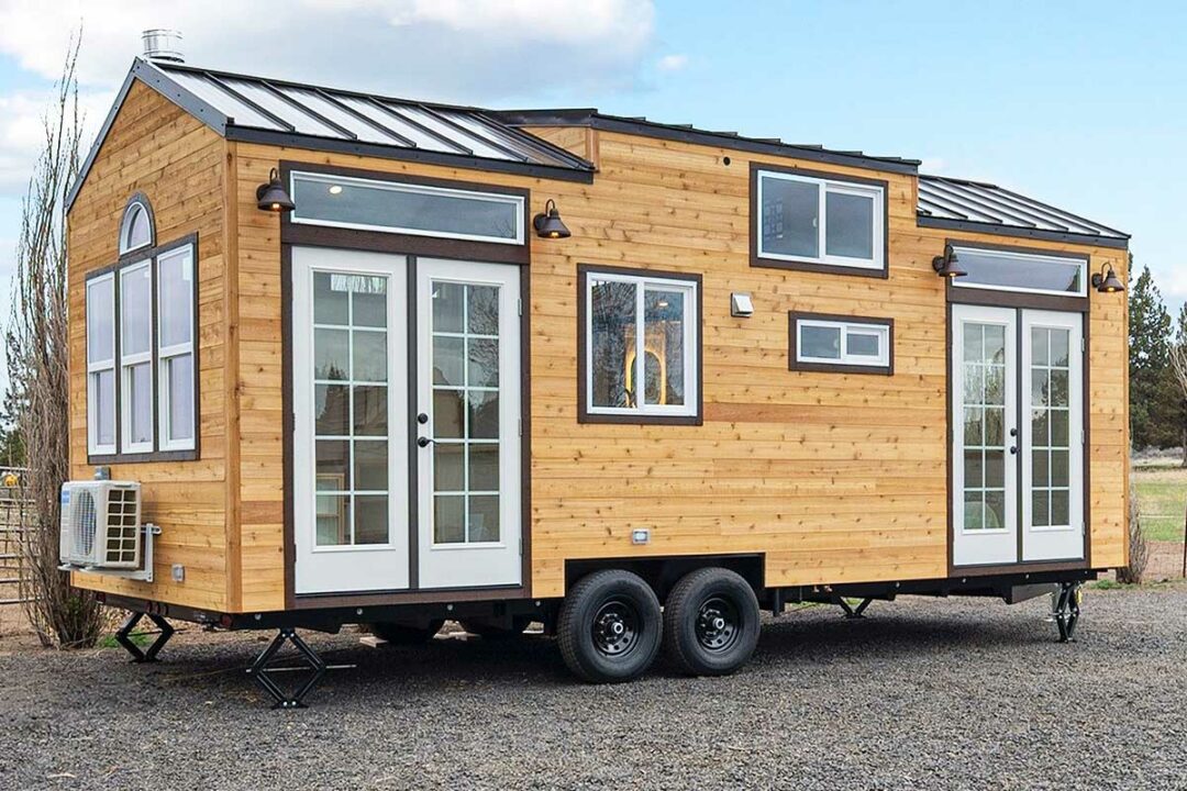 Une tiny house avec de multiples fenêtres sur une remorque à double essieu.