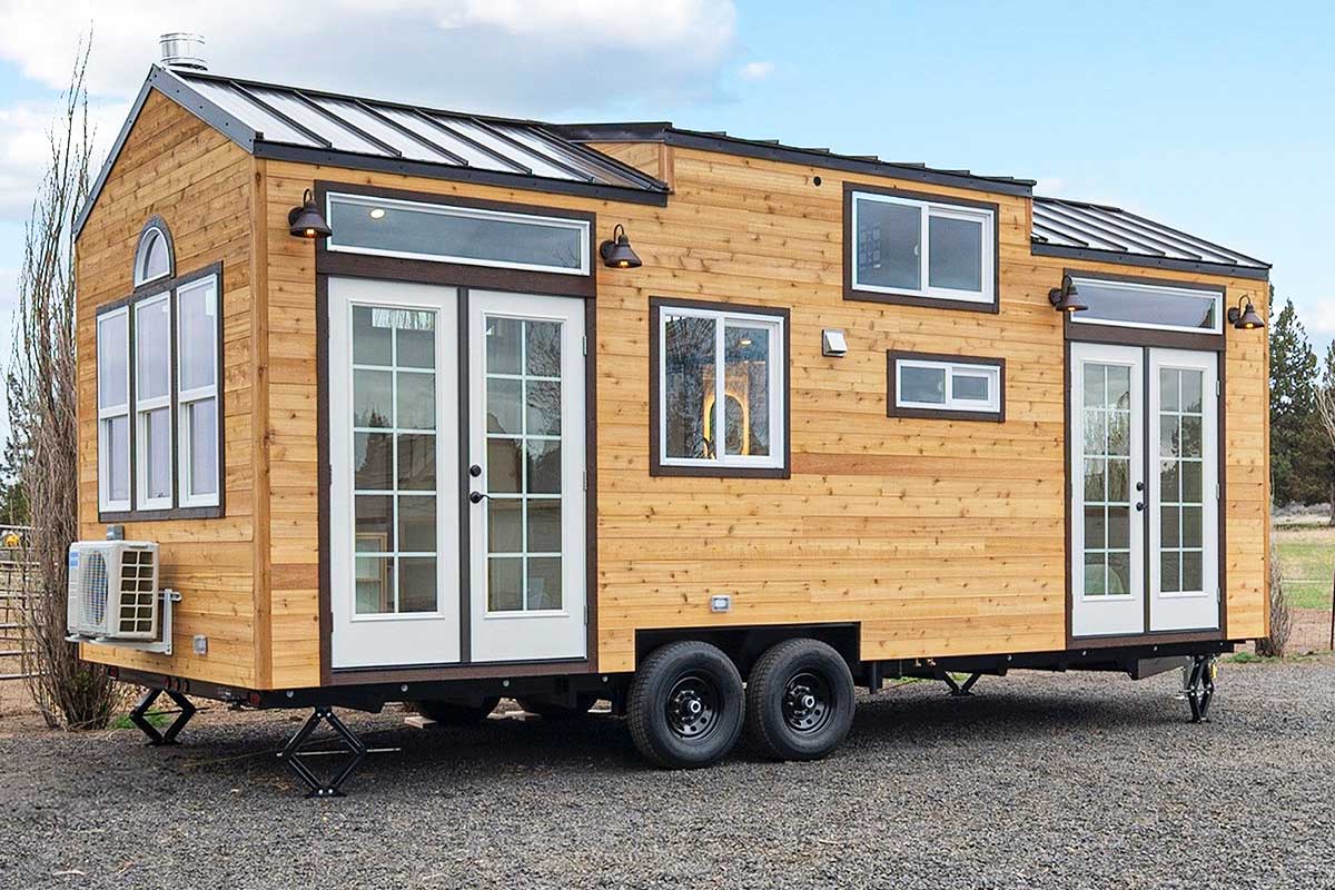 Une tiny house avec de multiples fenêtres sur une remorque à double essieu.