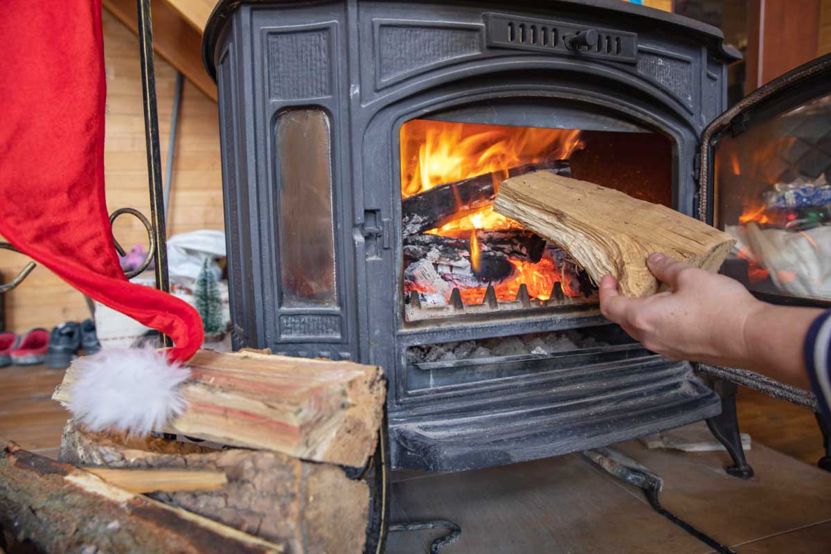 Une personne met une buche dans un poêle à bois.